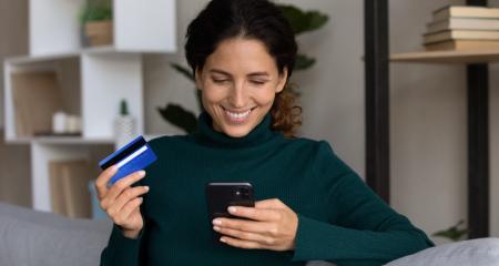 Happy millennial attractive woman holding banking card and cellphone in hands, feeling satisfied with secure internet payment, transferring money or paying for services, online shopping concept